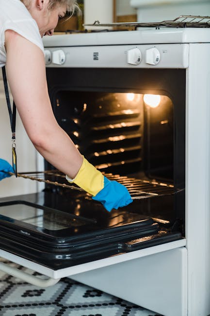 A close-up view of a domestic kitchen counter displaying a small, white oven with a stainless steel handle, situated on a wooden surface. The oven’s exterior appears slightly greasy, with a fabric c